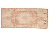 Vintage distressed Oushak runner with a scalloped medallion in faded rose, ivory, and charcoal.