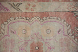 Detail of a geometric floral blossom in dusty rose and magenta on a distressed Oushak rug.