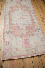 Angled perspective of a distressed Oushak runner with a faded, dusty rose medallion and low pile.