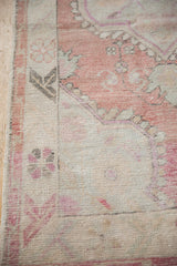 Low, hand-knotted pile on a distressed Oushak rug showing dusty rose and charcoal floral motifs.