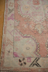 Worn pile on the corner of a distressed Oushak rug with a geometric floral border in dusty rose.