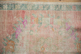 Low pile texture of a distressed Turkish Oushak with faded floral patterns in blush pink and dusty teal.