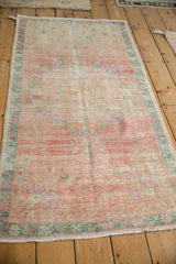 Angled view of a distressed Oushak runner with a soft pink field and dusty teal border.