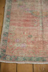 Corner view showing the dusty teal border and abrashed rose field of a distressed Oushak runner.