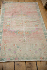 Angled view of a distressed vintage Oushak rug showing its soft, low pile and faded pink and teal palette.