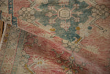 Rolled vintage distressed Oushak rug showcasing its textured pile and dusty rose, teal hues.
