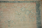 Worn hand-knotted pile on an Oushak rug corner with a thick teal border and dusty rose patterns.