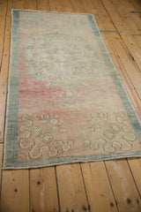 Angled view of a distressed Oushak runner with a faded dusty rose field and seafoam green border.