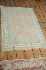 Angled view of a distressed Oushak rug with a pale melon field and soft seafoam green border.