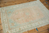 A distressed vintage Oushak rug from an angle, showing its soft melon and seafoam green colors.