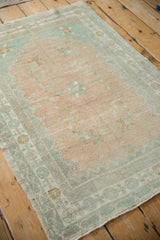 A vintage distressed Turkish Oushak rug shown at an angle in pale melon and seafoam green.