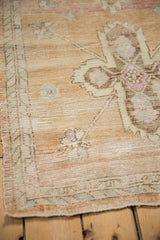Distressed Oushak rug corner highlighting abrashed pile, sand tones, and patterned minor border.