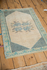 Distressed Oushak rug corner with ivory field, blue checkered spandrel, and turquoise border.