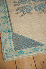 Distressed Oushak rug corner showing blue checkered spandrel and meandering vine border.