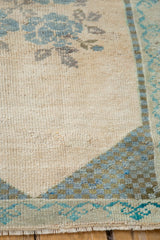 Vintage Oushak rug corner with blue checkered spandrel, ivory field, and visible fringe.