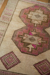 Geometric medallions in magenta and brown on the worn, low pile of a vintage Kars rug.
