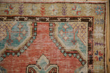 Brick red corner spandrel and floral border on a distressed Turkish Oushak rug showing textured wear.