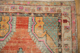 Corner of a distressed Oushak rug showing worn texture and a floral border with pink and orange.