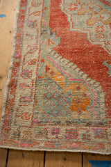 Corner detail of a distressed Oushak rug, showing its low-pile texture and colorful floral border.