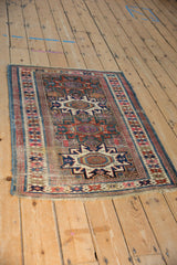 Antique Caucasian rug corner with geometric borders, worn fringe, and fuchsia color migration.