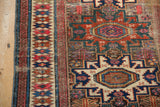 Storied geometric blossoms and borders of an antique Caucasian rug in ruby red, teal, and ivory.