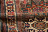 Folded antique Caucasian rug, geometric starburst motifs in sapphire, brick red, ivory.