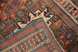 Detail of antique Caucasian rug's corner showcasing geometric patterns, fuchsia, teal, and secured side finish.