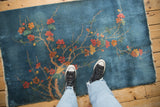 Feet on a vintage Chinese Art Deco rug showcasing sky blue field and blossoming branches.