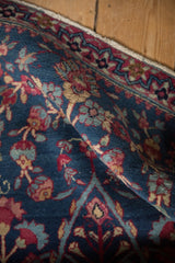 A close-up view of the softly folded pile of a fine antique Kerman rug in indigo, red, and sand.