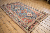 Long angle view of an antique Qashqai rug with a sapphire blue field and intricate geometric medallions.