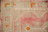 Evenly worn pile of a vintage Oushak rug with rose, sea foam green, and tangerine geometric details.