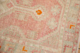 Worn pile of a distressed Oushak rug with geometric patterns in blush, seafoam, and tangerine orange.