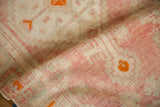 A folded view showing the textured, low pile of a distressed Oushak rug in blush and orange.