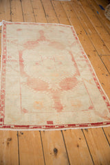 Distressed Oushak rug corner, showing faded cochineal red geometric border and subtle wear.