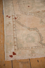 Distressed vintage Oushak rug corner with even wear, intact selvage, and cream, green, rust tones.