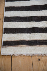 Plain-weave texture of a vintage kilim, showing horizontal platinum and charcoal stripes with fringe.