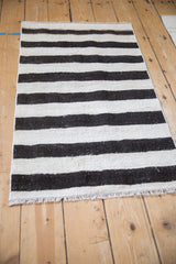 Bottom edge of a Turkish Hemp Kilim rug showing charcoal and ivory stripes and fringe.