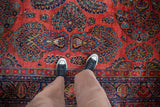 Hand-knotted vintage Sarouk rug with brick red field, dense floral sprays, and blue palmettes.