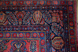 Vintage American Sarouk rug corner with brick red field, navy border, sapphire palmettes, and floral sprays.
