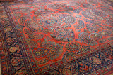 Angled view of American Sarouk rug's brick red field, dense floral sprays and navy border.