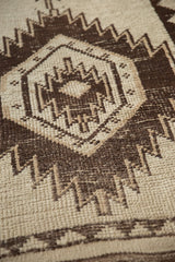 Vintage Kurd rug's geometric zig-zag pattern in chocolate brown on ivory with visible knot heads.