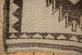 Vintage Kurd rug corner showing geometric ivory and brown pattern, braided selvage, and shorn pile.