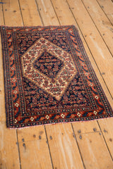 Angled view of a vintage Persian Senneh mat highlighting its stepped navy medallion and red borders.