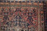 Detail of antique Senneh rug's navy border and brick red field, with tattered selvedge.