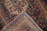 Intricate Herati design in navy, brick red, sand; worn pile and raw edge of antique Senneh rug.