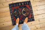 A person provides scale for the small antique Malayer rug with red and blue design.