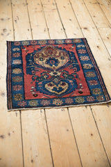 Angled view of a square antique Malayer rug with red and sapphire blue palmette medallions.