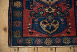 Corner of an antique Malayer rug with a blue floral border, intact side selvage, and short knotted fringe.