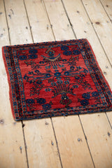 A small antique Sarouk sampler rug viewed at an angle, showing its gem-like ruby and sapphire tones.