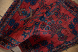 Angled close-up of a folded antique Sarouk rug, showing the pile texture and rich ruby red color.